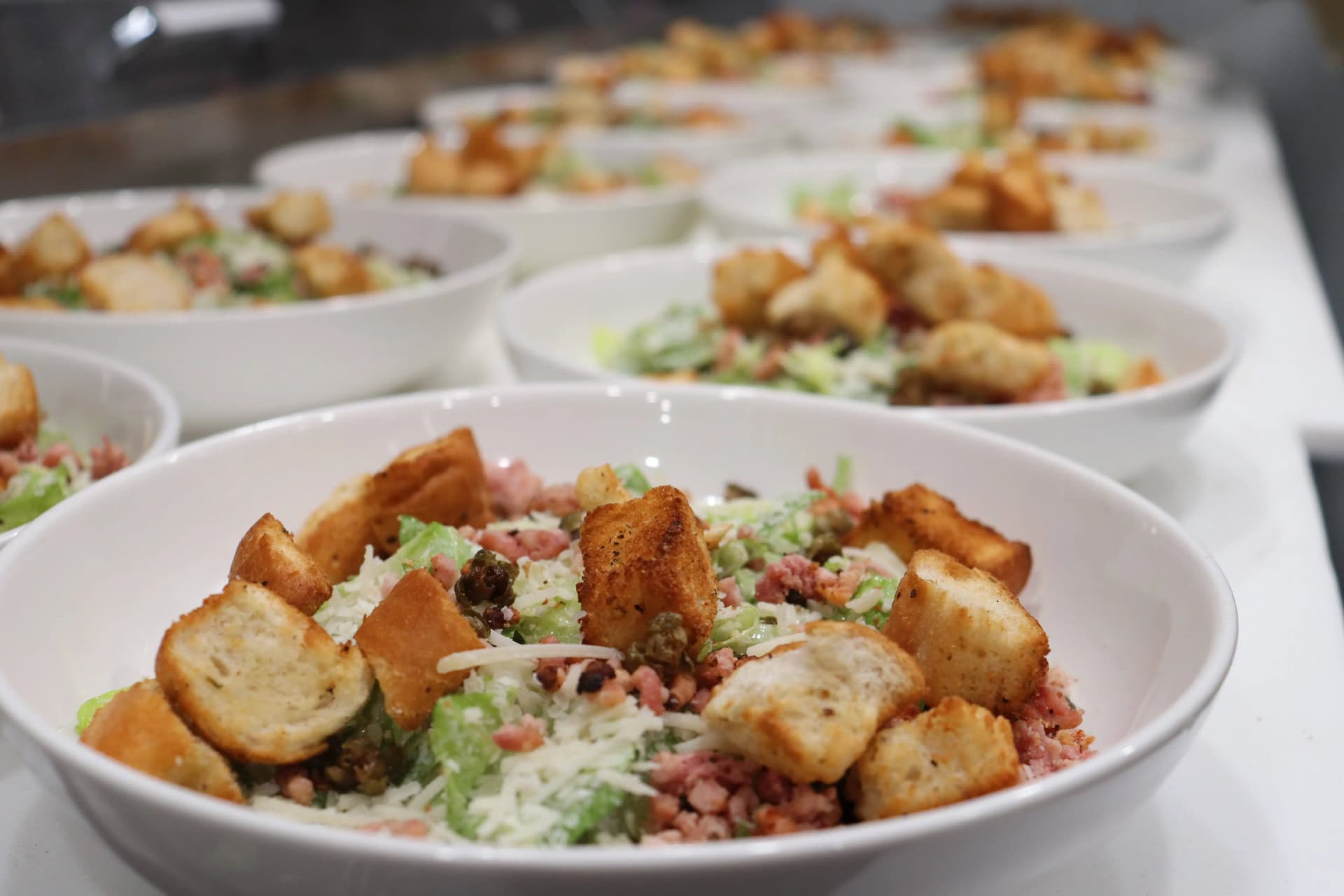 Multiple caesar salad plates with house-made croutons, parmesan cheese, and bacon crumble